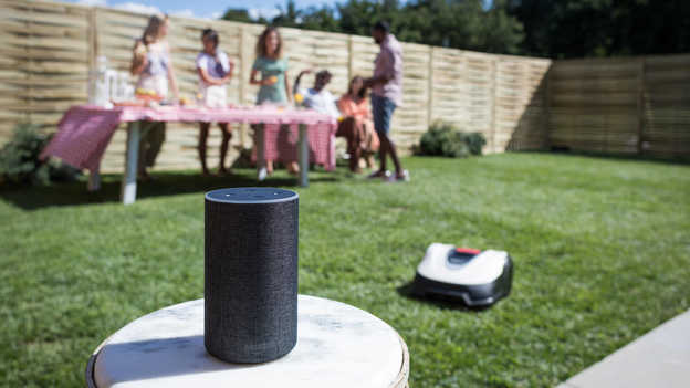 Primo piano di Amazon Alexa con Miimo e festa in giardino sullo sfondo sul prato.
