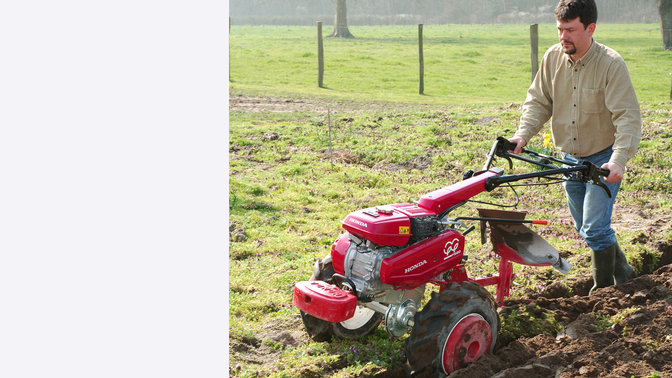 Versatile tiller with plough attachment, being used by model, garden location.
