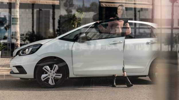 Vista laterale di Honda Jazz parcheggiata con una signora che apre la portiera