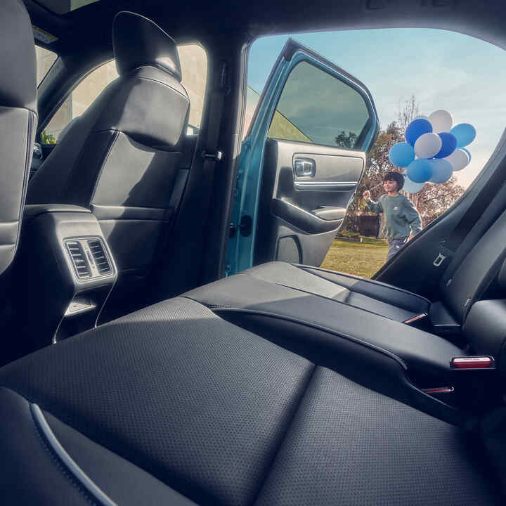 Primo piano del sedile posteriore di un Honda e:Ny1 con un bambino che passa accanto alla portiera aperta con dei palloncini.