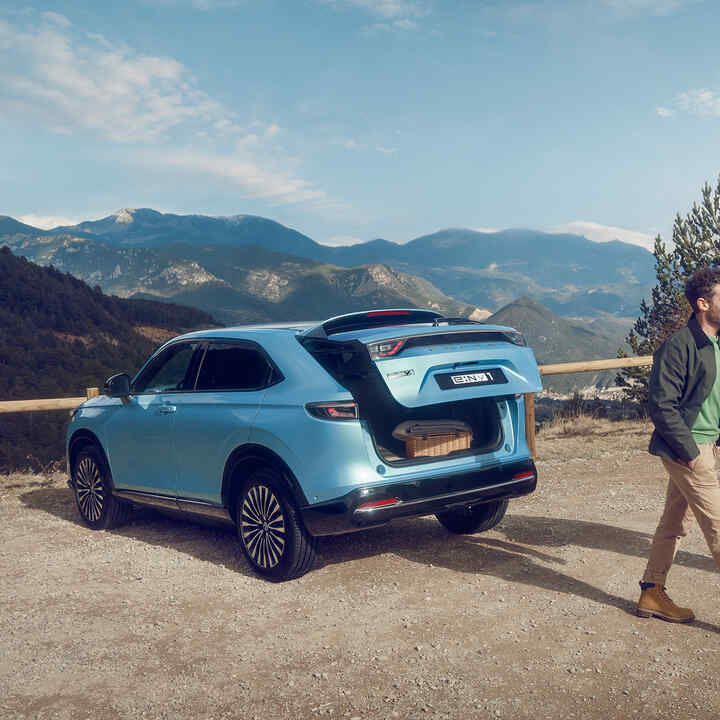 Vista posteriore di tre quarti di un Honda e:Ny1 in un ambiente montano con una coppia che si allontana.