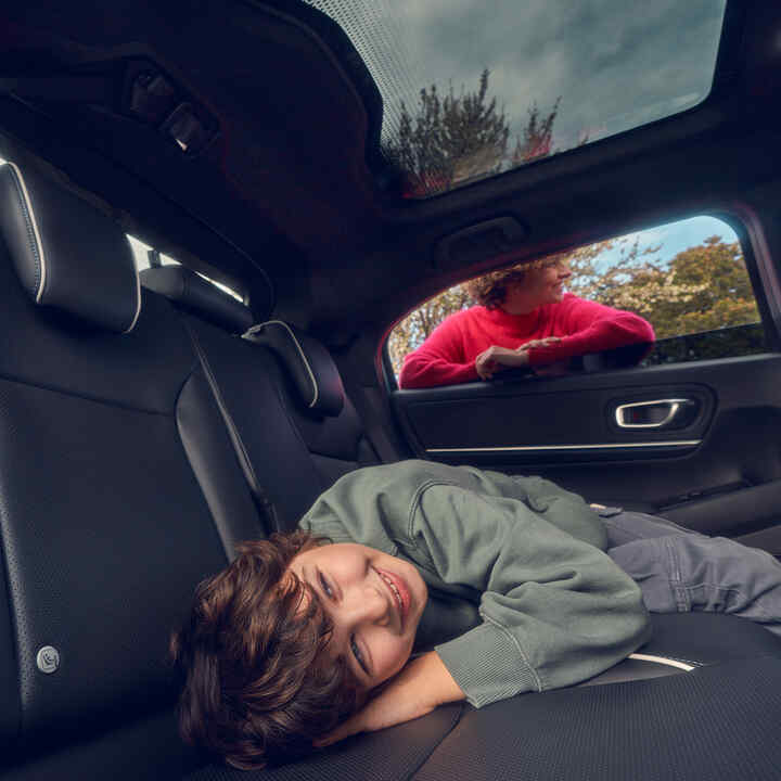 Bambino sdraiato sul sedile posteriore mentre la madre sta in piedi davanti al finestrino di un Honda e:Ny1.