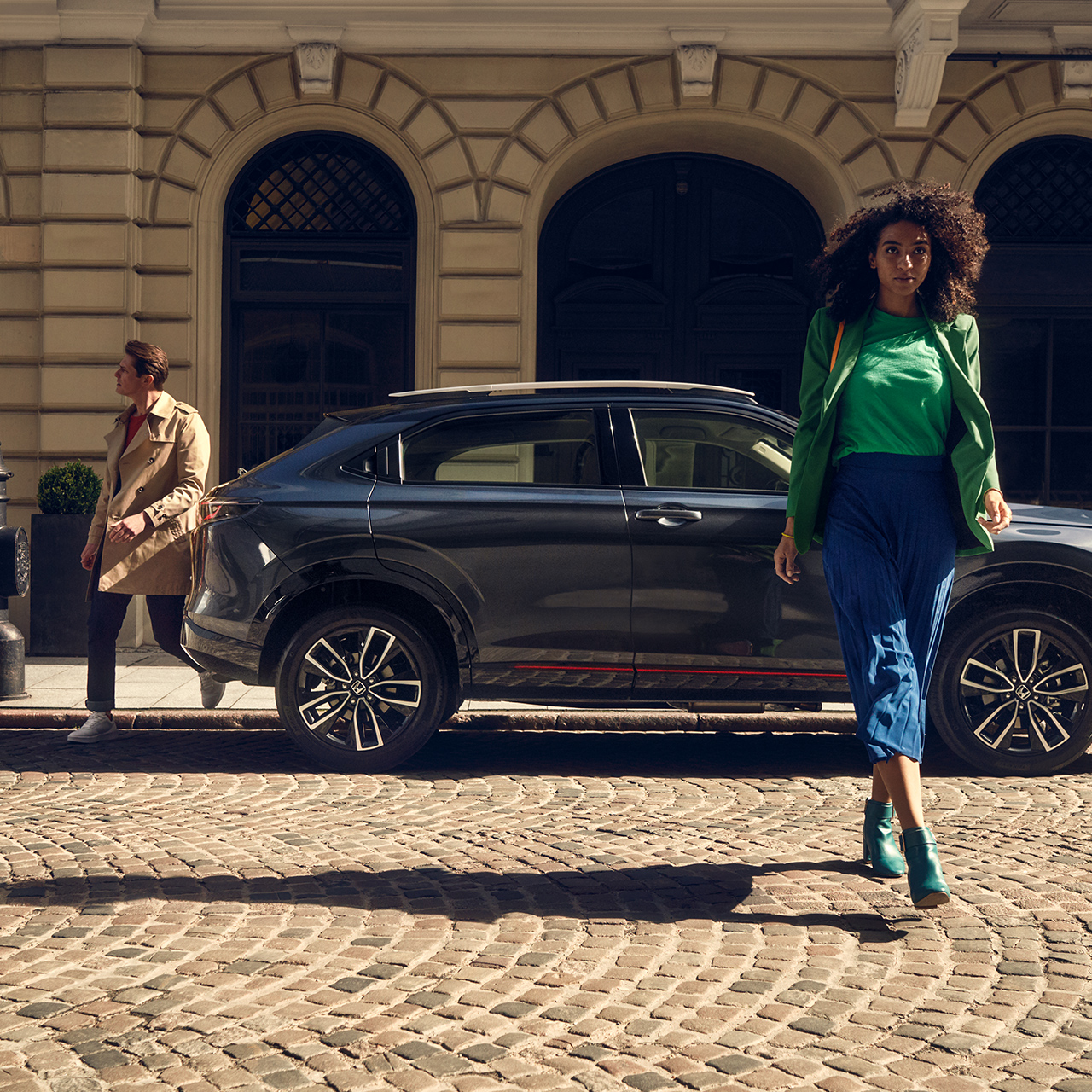 Modello che cammina davanti a HR-V Hybrid parcheggiato in città.