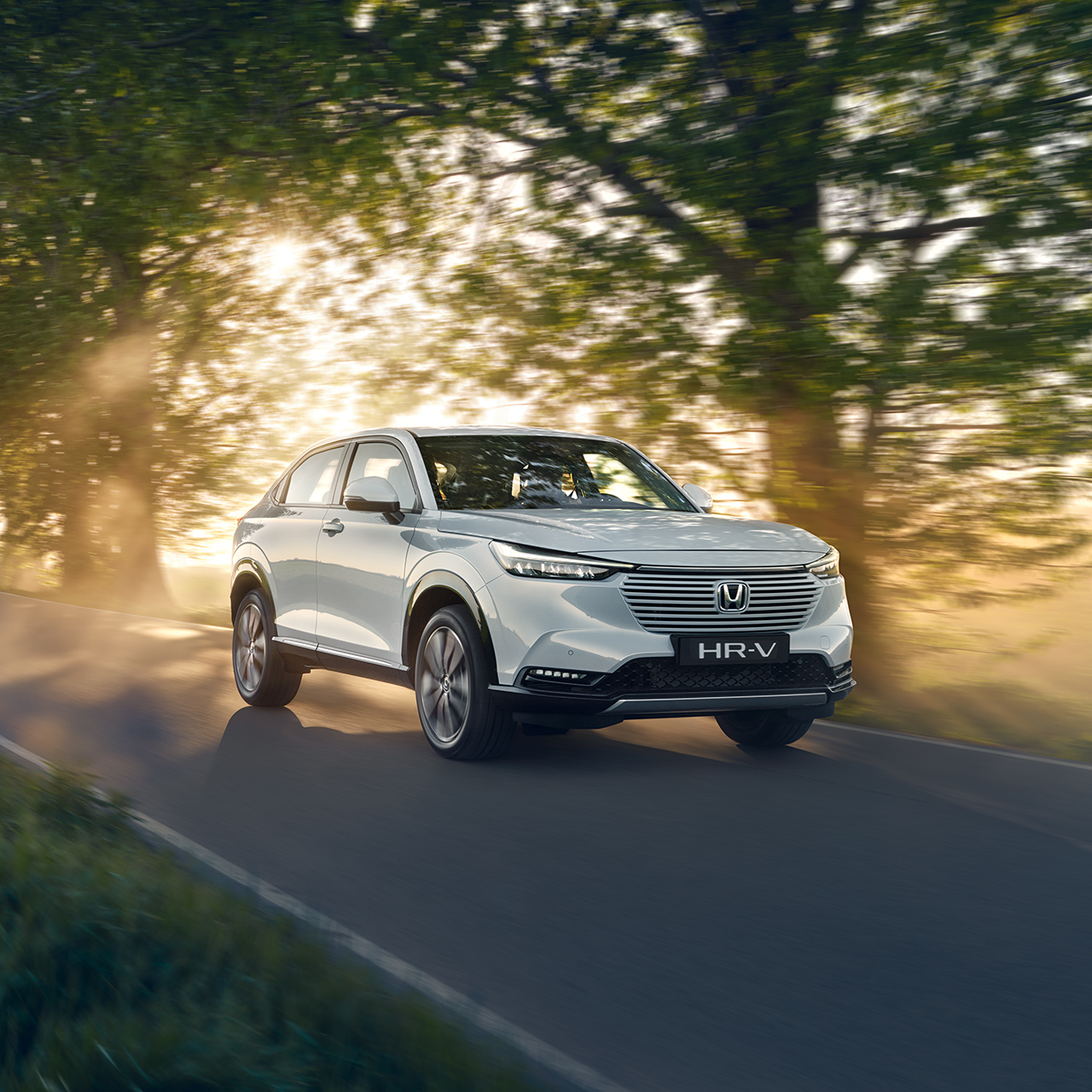 HR-V Hybrid in marcia su strada in un ambiente di campagna.
