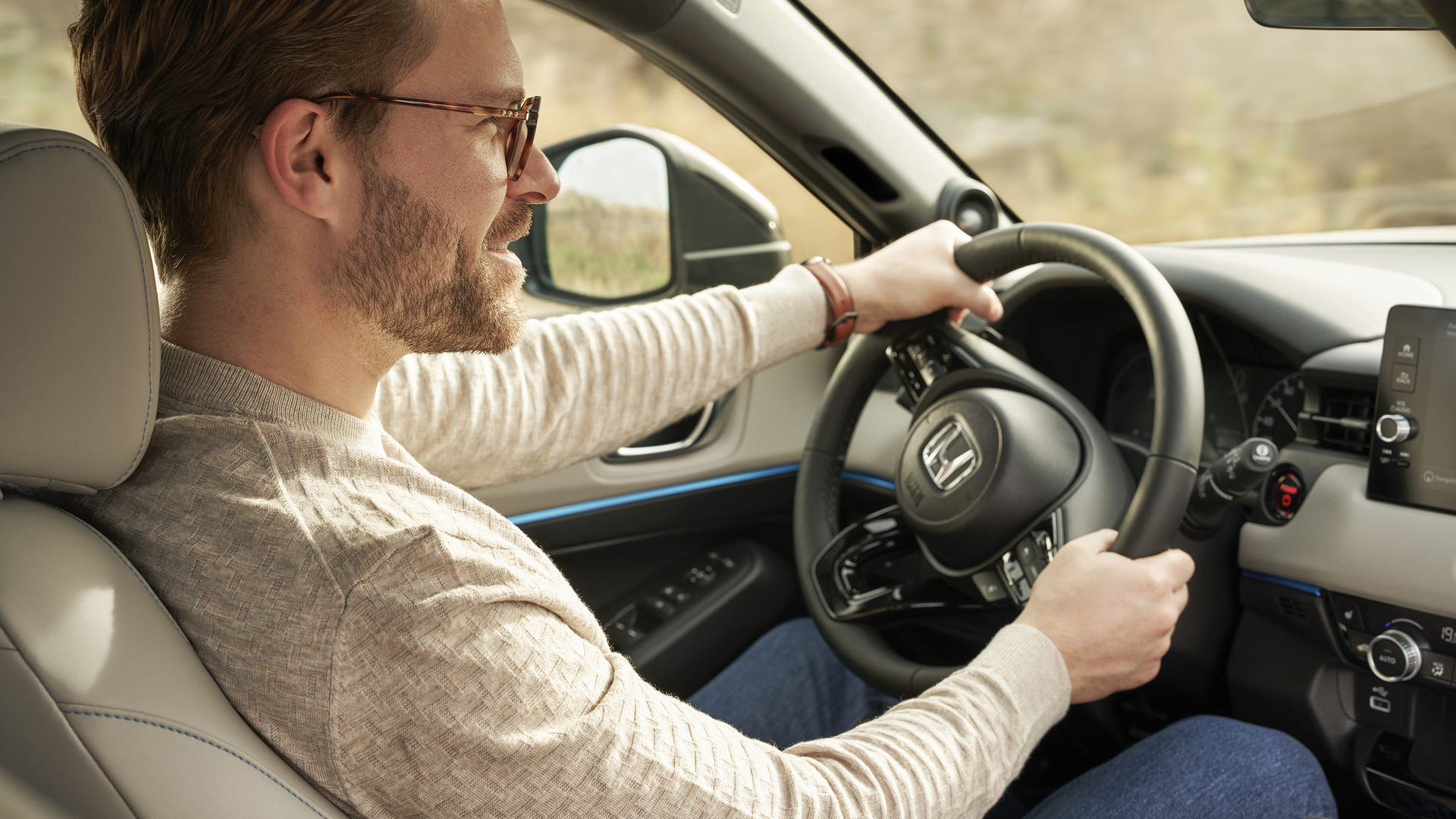 Un uomo con gli occhiali guida una Honda HR-V, visto dal sedile del passeggero anteriore, con entrambe le mani sul volante e la plancia visibile.