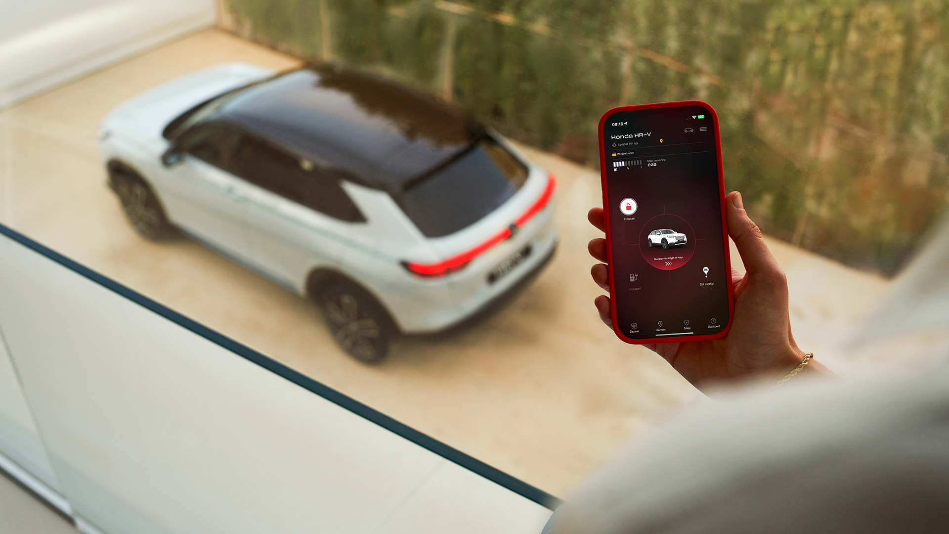 Una persona tiene in mano uno smartphone che mostra un'app per le impostazioni di ricarica del veicolo, mentre sullo sfondo è parcheggiato un SUV bianco.