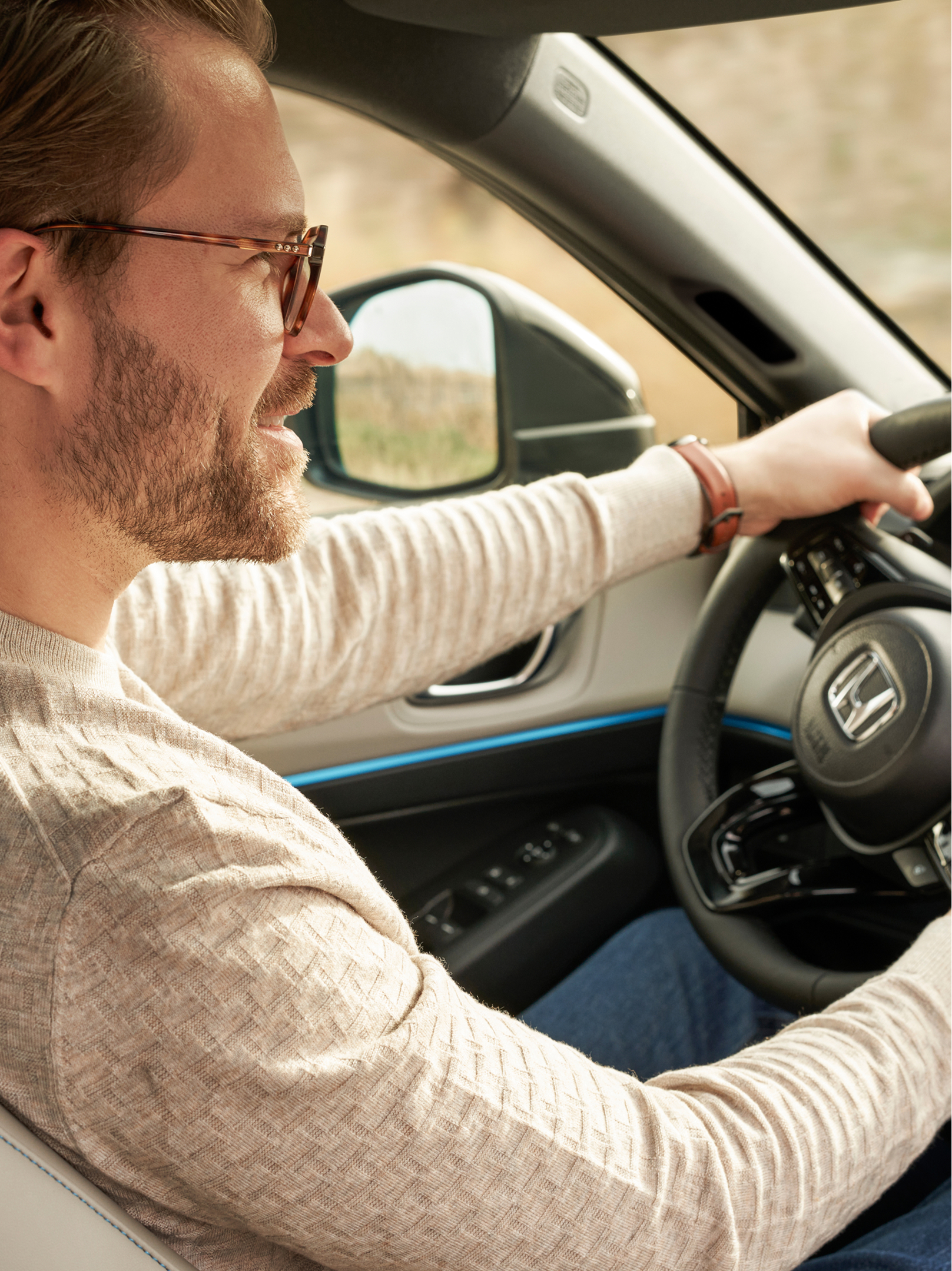 Un uomo con gli occhiali guida una Honda HR-V, visto dal sedile del passeggero anteriore, con entrambe le mani sul volante e la plancia visibile.