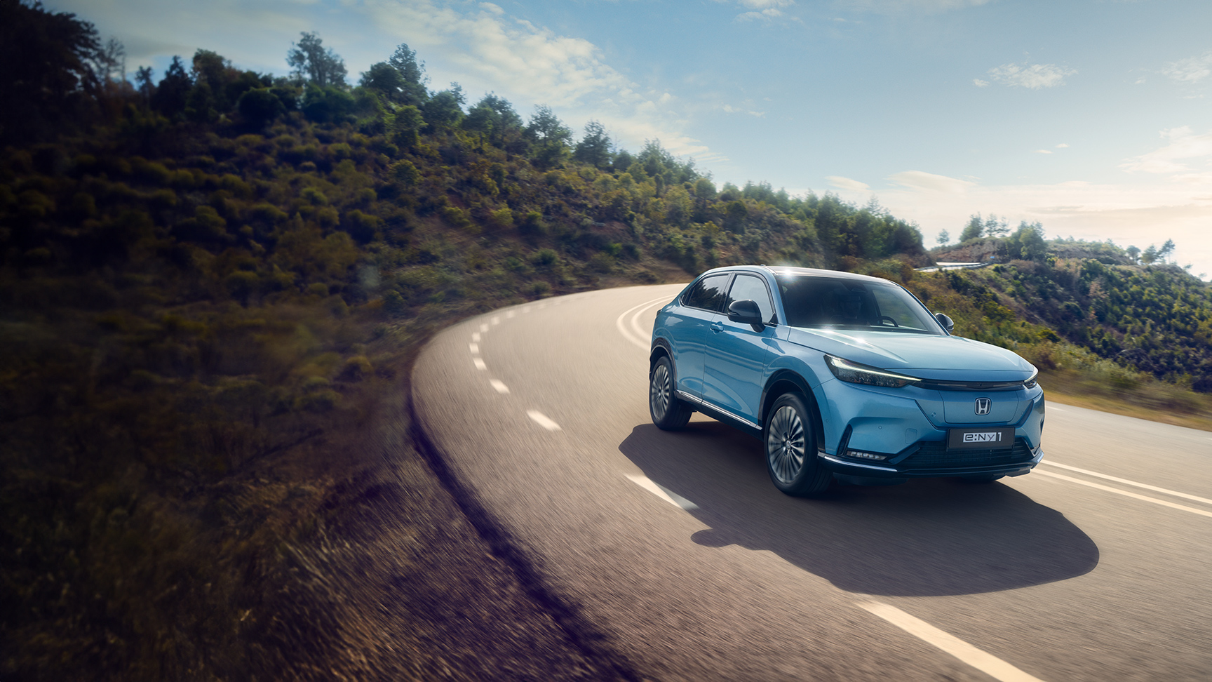 Vista frontale di tre quarti di Honda e:Ny1 guidata in un ambiente montano. 
