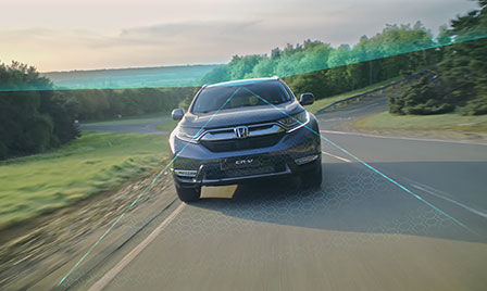 Honda Sensing car in a countryside location with illustration of road departure mitigation and traffic sign recognition.