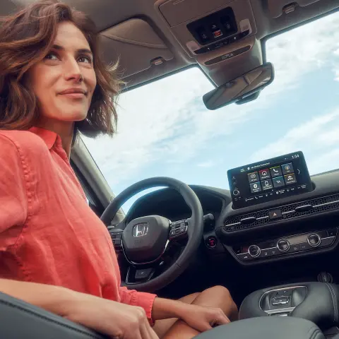 Donna seduta al posto di guida mentre utilizza lo schermo del sistema di infotainment di Honda ZR-V Hybrid.