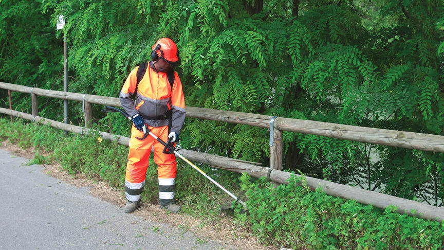 Modello con decespugliatore spalleggiato in un ambiente boschivo.