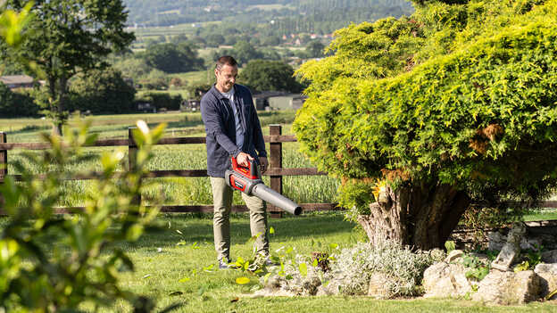 Uomo che tiene e utilizza un soffiatore a batteria in giardino