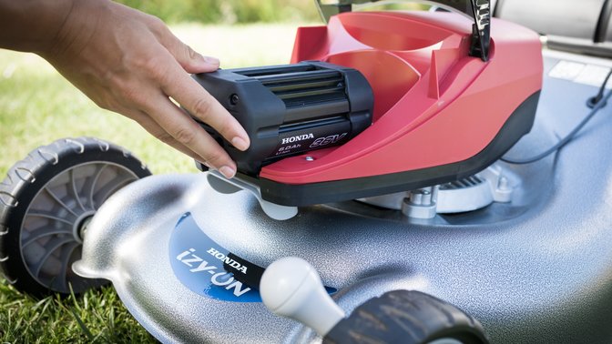 Model hands changing battery of Honda izy-ON mower.