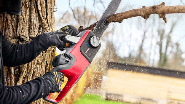 Primo piano di un modello che taglia il ramo di un albero con una motosega a batteria.