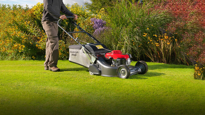 Uomo con il rasaerba Honda HRH che taglia l'erba in giardino