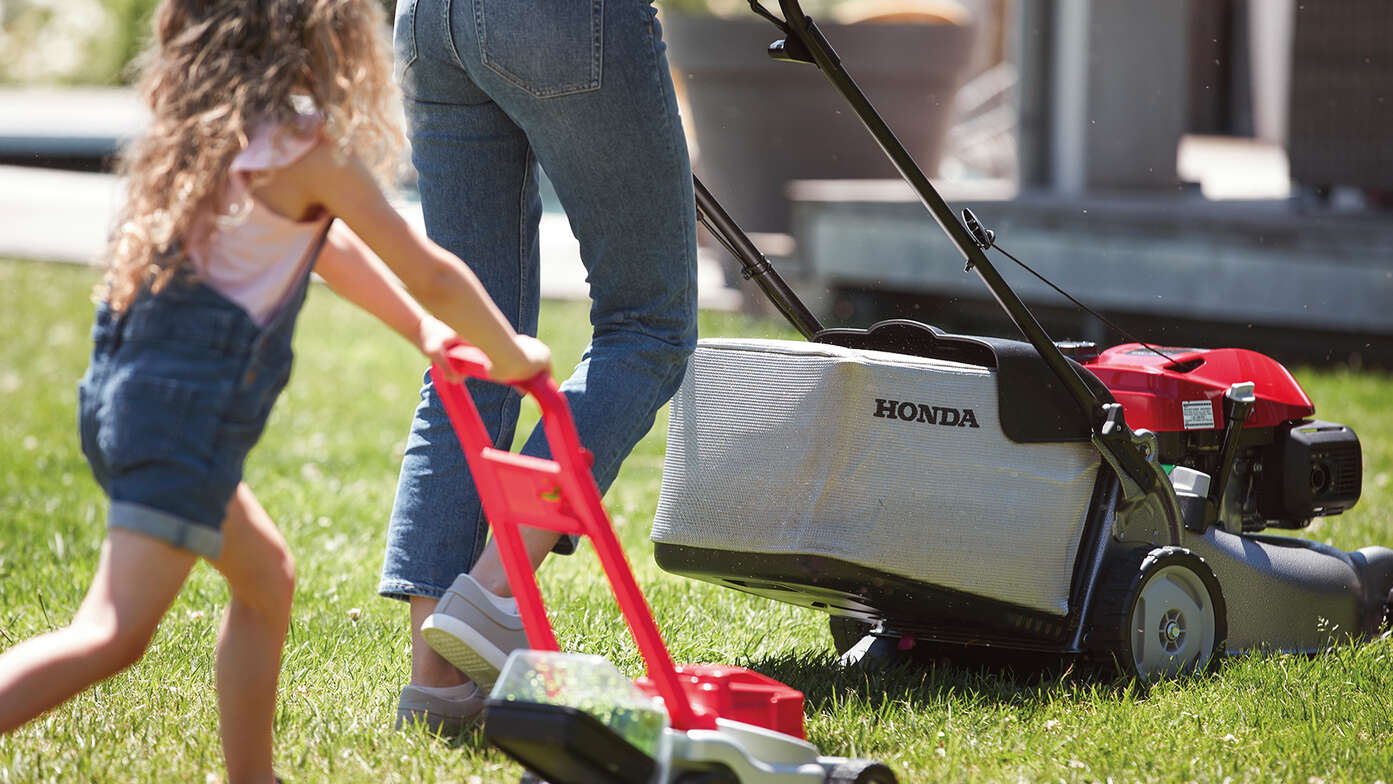 Vista laterale del rasaerba Honda IZY con una donna e un bambino in giardino