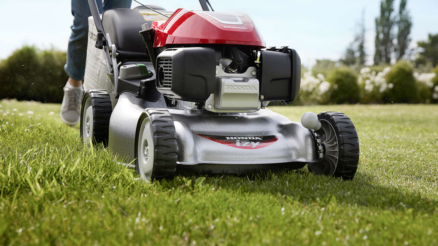 Vista laterale del rasaerba Honda IZY con una donna in giardino