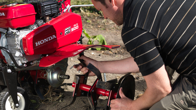 Operatore che collega un nuovo accessorio ad una motozappa compatta, luogo di utilizzo: giardino.