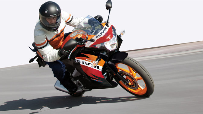Inquadratura frontale di tre quarti della Honda CBR125R con il pilota piegato in curva. Lato destro (su strada).