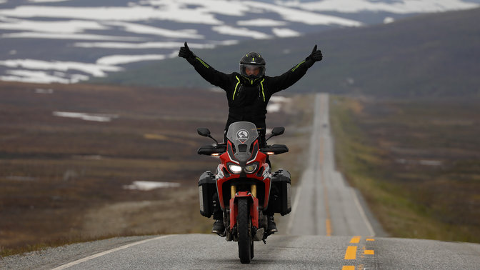 Uomo su una Honda Africa Twin con le braccia alzate sulle strade di Nordkapp.