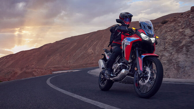 Modello che guida la moto CRF1100L Africa Twin su una strada in una località di montagna.