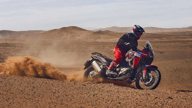 Modello alla guida di una moto CRF1100L Africa Twin in un luogo desertico.