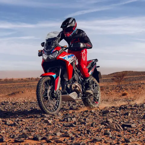 Modello che guida la moto CRF1100L Africa Twin su un terreno roccioso in una località desertica.