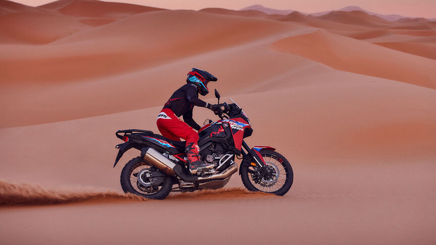 Modello in sella a una moto CRF1100L Africa Twin in un luogo desertico.