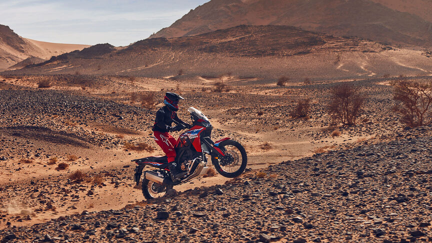 Modello in sella a una moto CRF1100L Africa Twin in un luogo desertico.