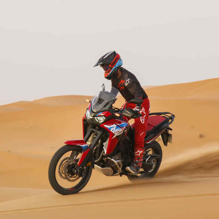 Modello che guida la moto CRF1100L Africa Twin su una strada in un luogo desertico.