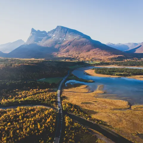 Classica vista scandinava/norvegese estiva di un paesaggio montano con strada, montagne e fiordo e sul fondo un cielo blu, Norvegia settentrionale, contea di Finnmark, ripresa da drone