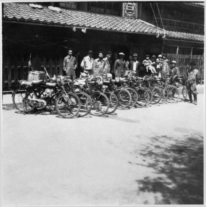 Una fila di 13 motociclette Honda del passato in Giappone con persone in piedi dietro di esse
