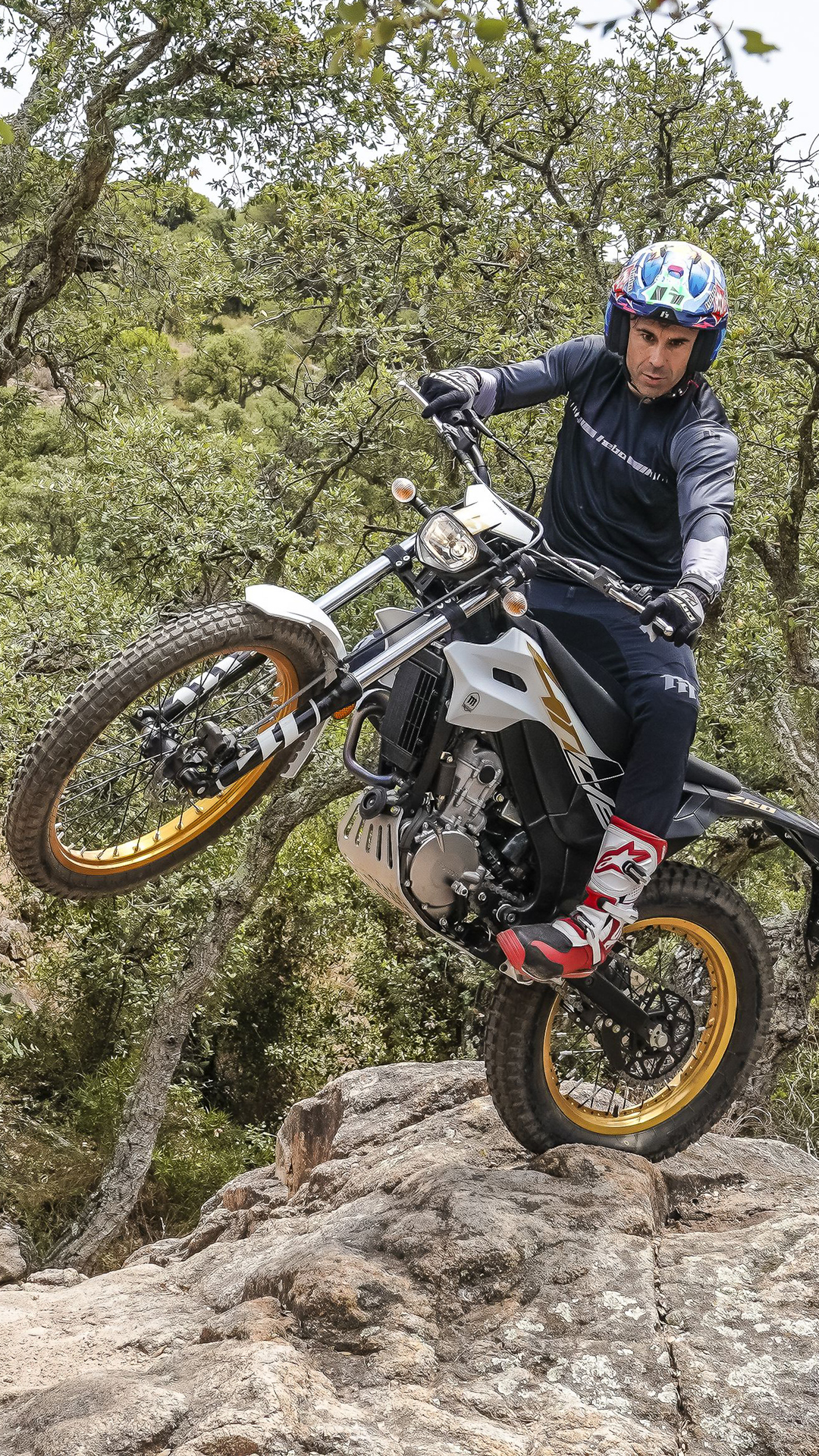 Un motociclista solleva la ruota anteriore di Montesa 4RIDE su un sentiero roccioso nel bosco.