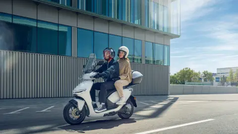 Modelli alla guida dello scooter elettrico Honda CUV e: in una location urbana.