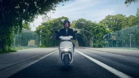 Vista frontale di un modello alla guida di uno scooter elettrico Honda CUV e: in un contesto urbano.