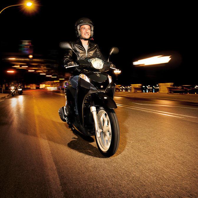 Scooter Honda SH Mode nero, inquadratura anteriore di tre quarti con guidatore. Lato destro (su strada).