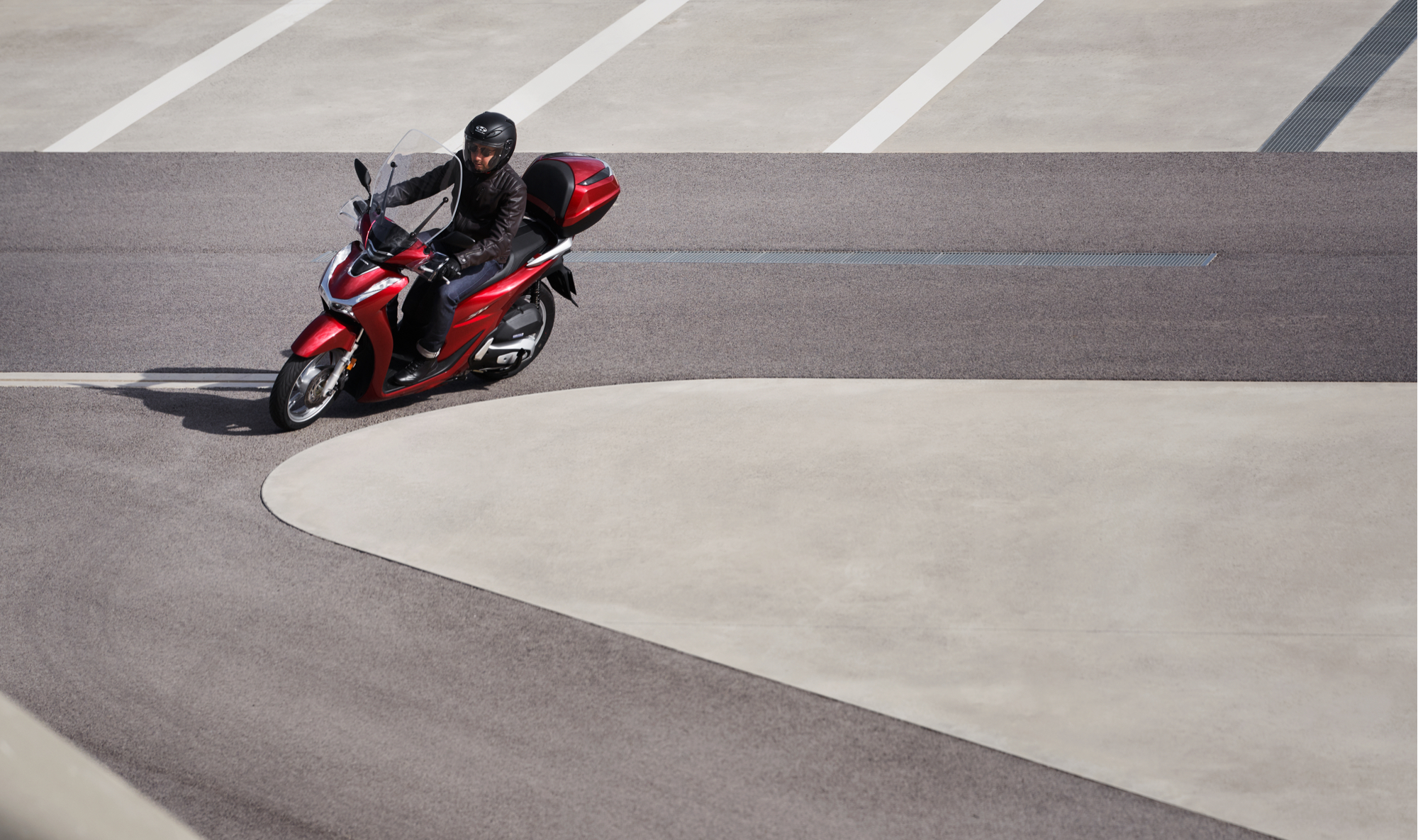 Honda-SH125i, inquadratura anteriore sinistra di tre quarti, con pilota, mentre svolta a sinistra in strada