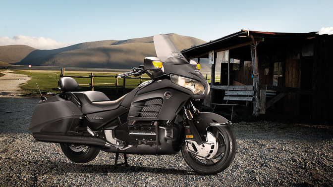 Inquadratura anteriore di tre quarti della Gold Wing F6B, parcheggiata, con pilota appoggiato sulla moto. (Ambiente rurale).