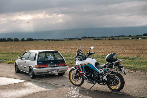 Una vecchia Civic e una moto Honda parcheggiate davanti a un campo