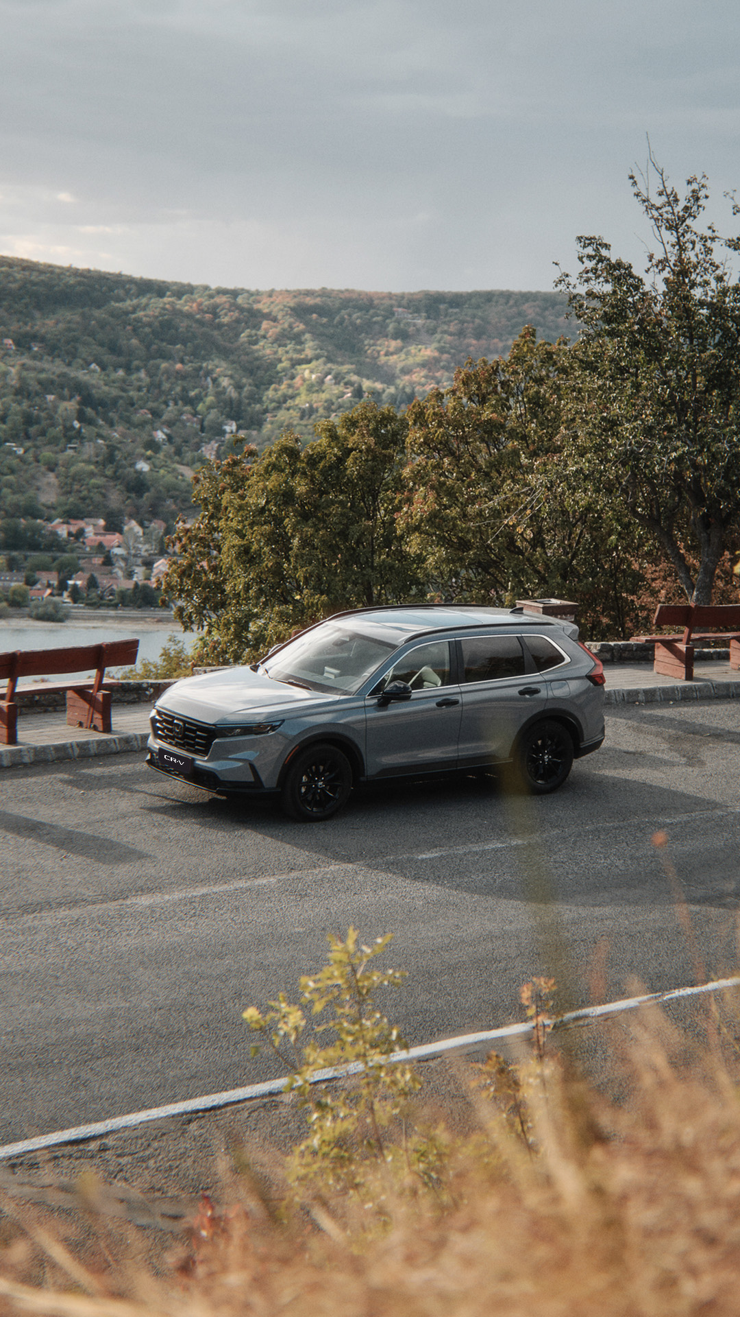 Un CR-V grigio che percorre una strada in riva al lago, con le montagne sullo sfondo